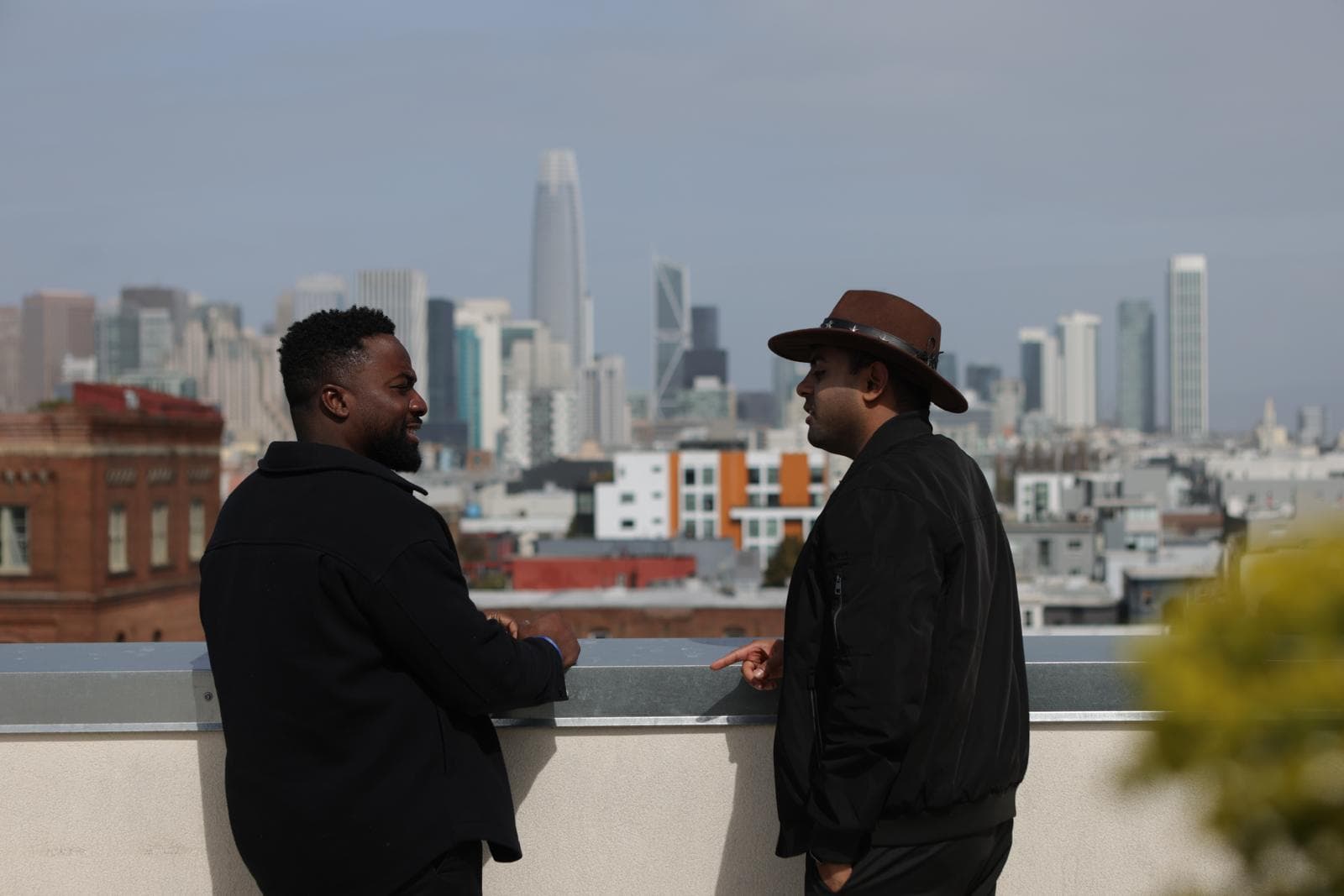 Papa talking with a guest on a San Francisco rooftop, Salesforce Tower behind them.
