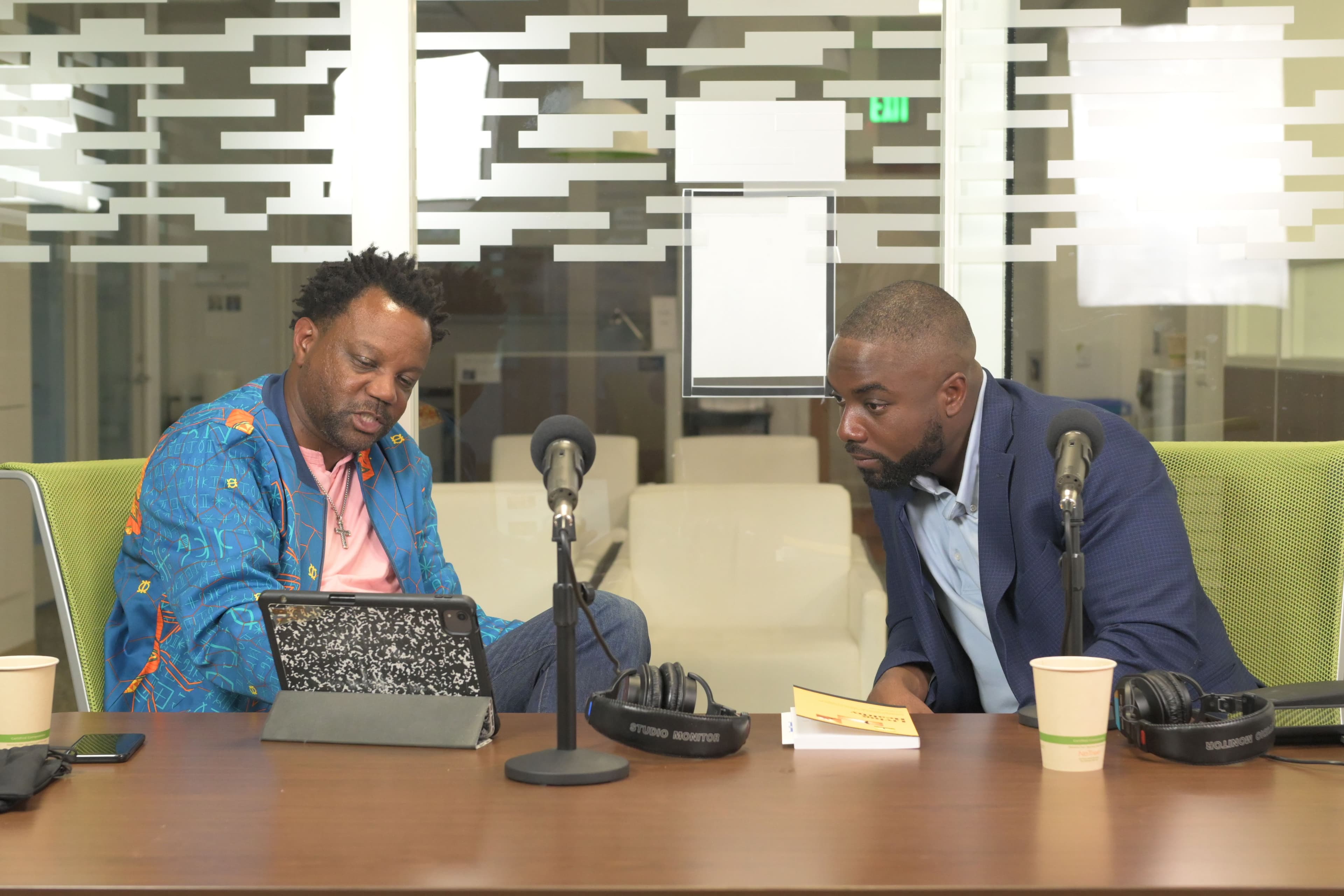 Guest Erick and Papa leaning over notes at a recording table between two microphones.